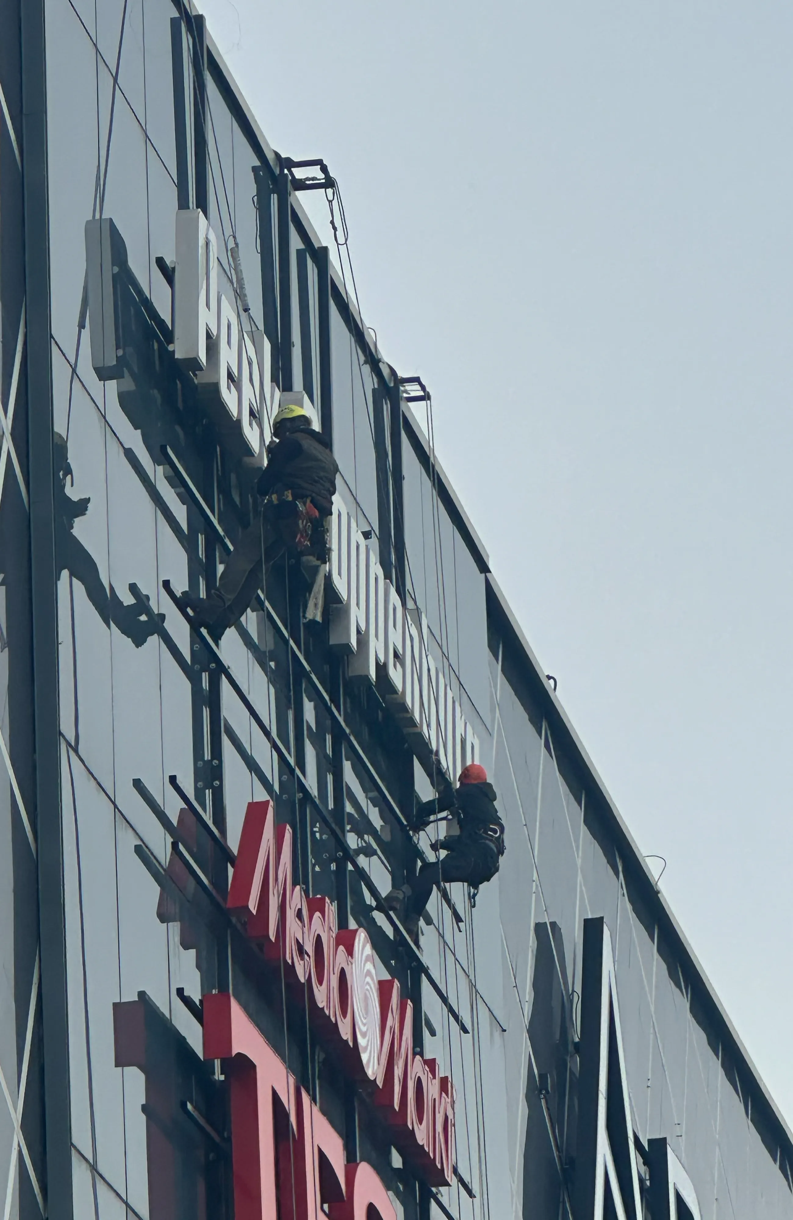 Op deze foto zie 2 mensen van RW Projecten aan het werk met een montage opdracht. Ze hangen aan een gebouw vast met veiligheidsvesten.